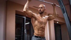 A bald, muscular man performing exercise on gym equipment indoors.